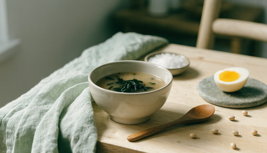 A bowl of miso soup with seaweed, whole soybeans, sea salt and a halved egg on a light oak table, illustrating soy and thyroid-supporting iodine foods