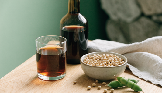 A glass of nitrogen fermented soy beverage beside a bowl of organic soybeans, representing Haelan 951, also known in research as FSWW08.