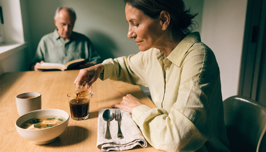 A woman pours a small glass of fermented soy beverage at a sunlit oak breakfast table beside a bowl of miso soup, illustrating the best time to eat fermented foods